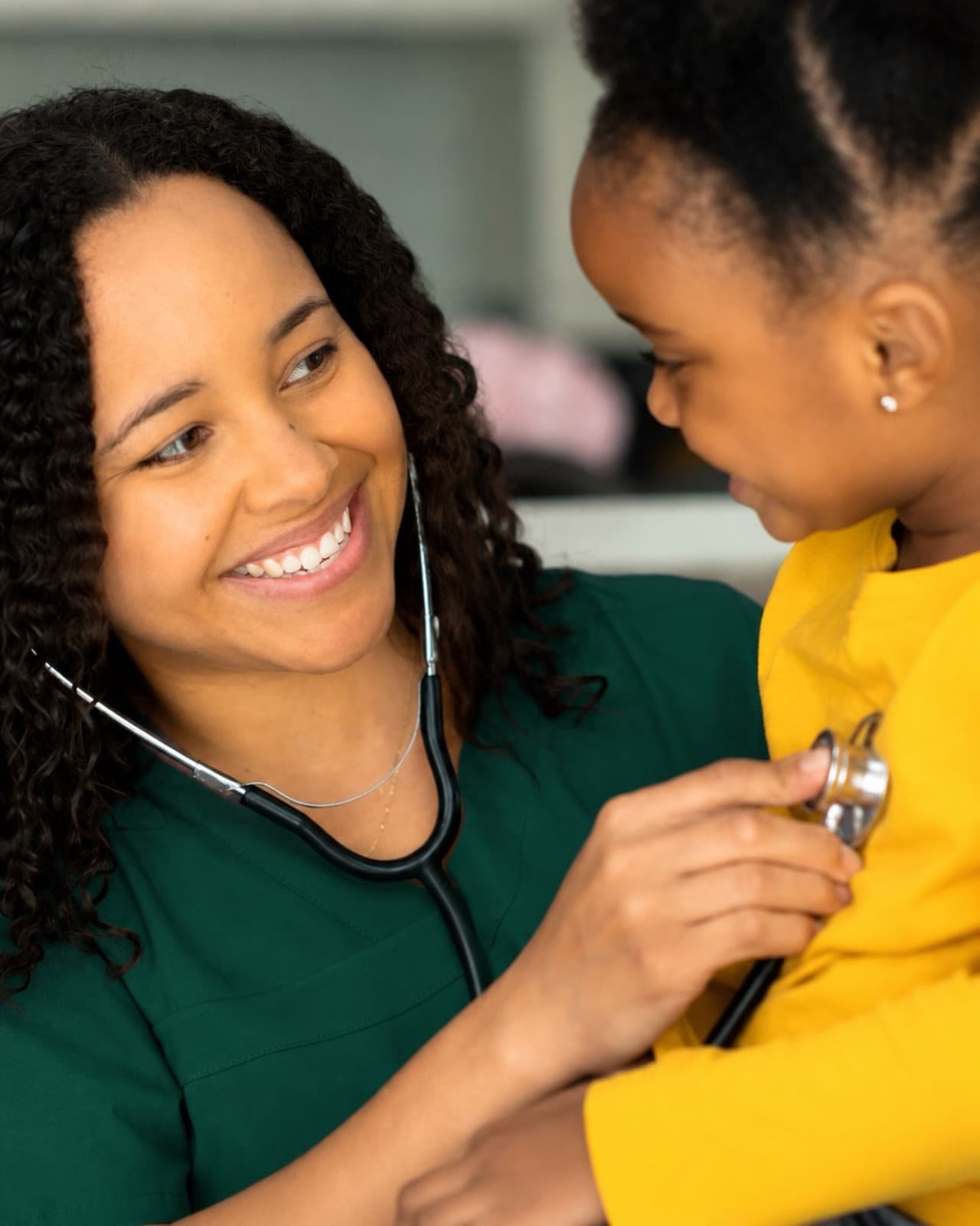 A smiling nurse checking a child's heartbeat